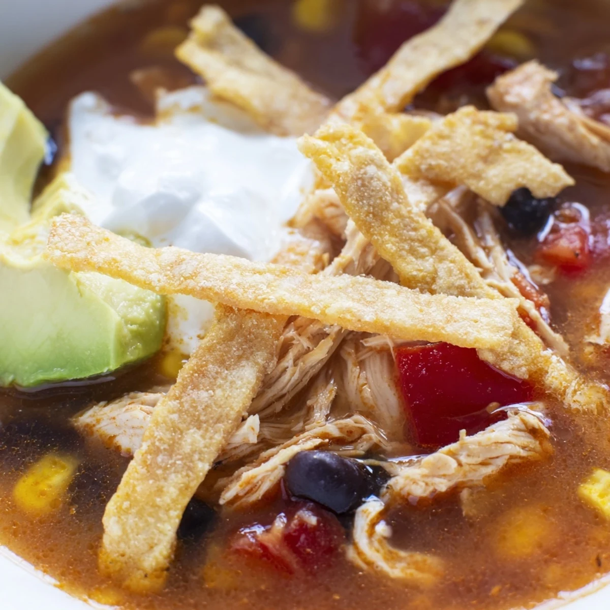 A comforting bowl of Chicken Tortilla Soup topped with creamy avocado slices, fresh cilantro, and a lime wedge on the side.