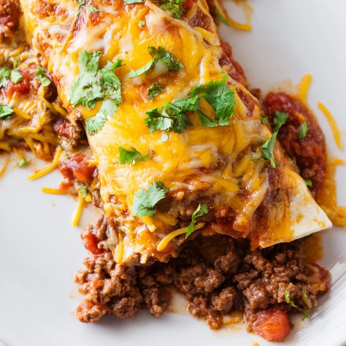 Serving of delicious Beef Enchiladas with red sauce on a plate with a side of rice.