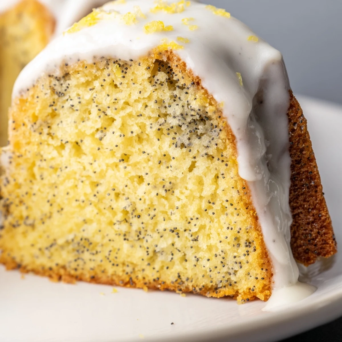 A freshly baked Lemon Poppy Seed Bundt Cake cooling on a wire rack, with a glossy lemon glaze dripping down its fluted ridges. This moist, tender Bundt cake bursts with fresh lemon flavor, dotted with crunchy poppy seeds, and topped with a zesty lemon glaze, perfect for brunch or as a light, refreshing dessert.