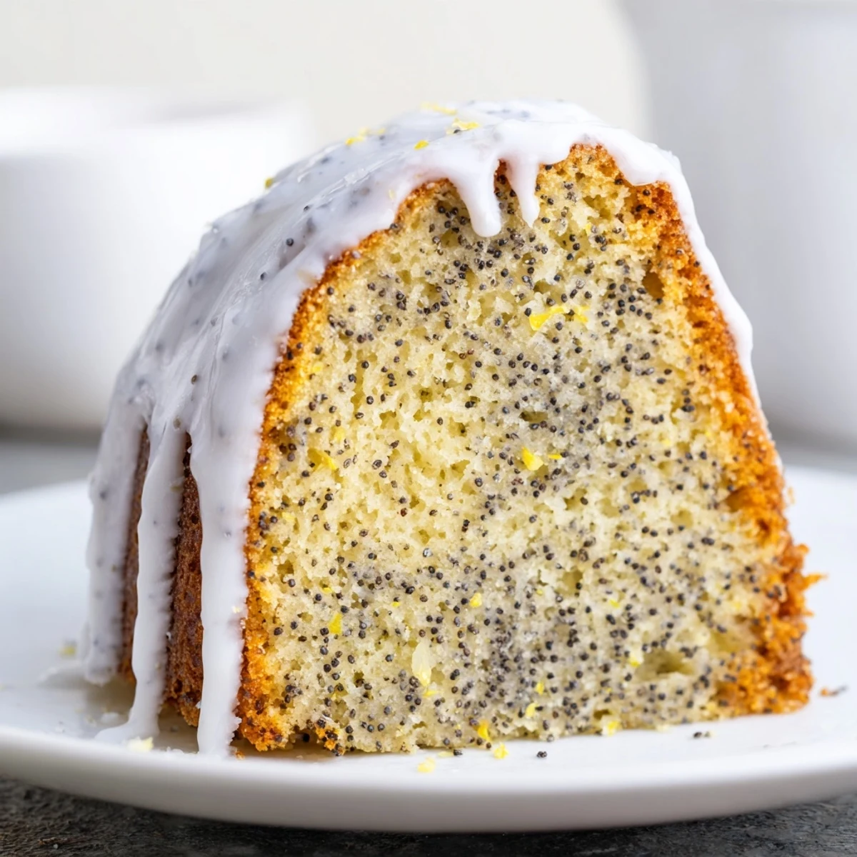Close-up of a slice of Lemon Poppy Seed Bundt Cake on a dessert plate, revealing a tender crumb with poppy seeds and a drizzle of lemon glaze. The moist, tender Bundt cake bursts with fresh lemon flavor and is topped with a zesty lemon glaze, ready to enjoy.