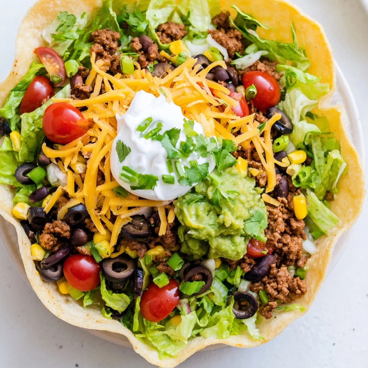 A warm Beef Taco Salad with Shell topped with sour cream, guacamole, and shredded cheddar for a creamy finish.