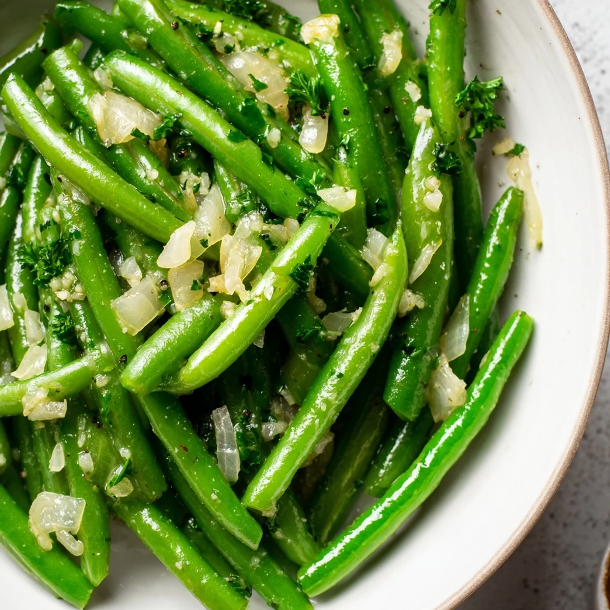Sautéed Garlic Butter Green Beans with fresh shallots and parsley garnish on a white plate.