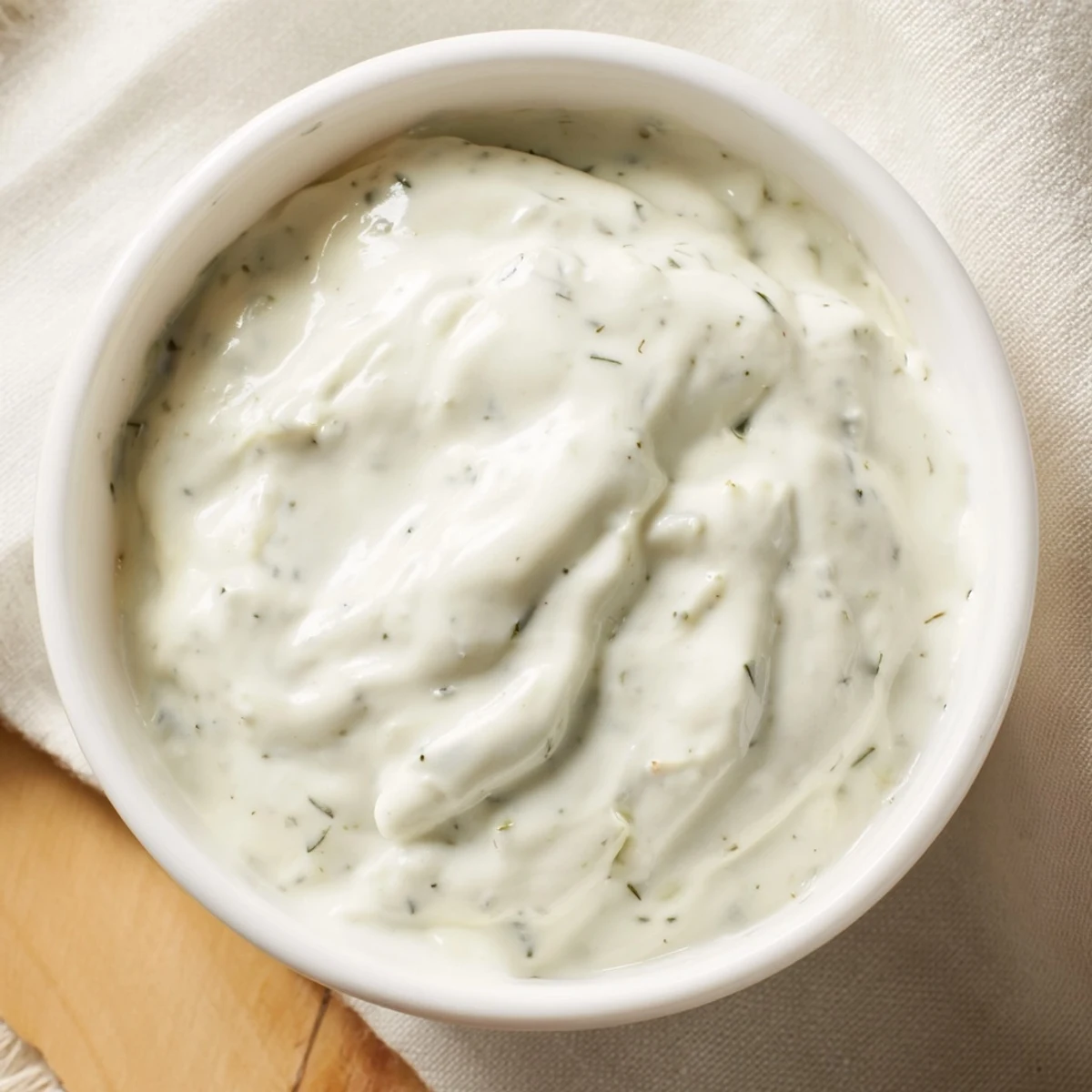 Creamy Herb Dressing in a white bowl, surrounded by fresh parsley and dill with lemon wedges.