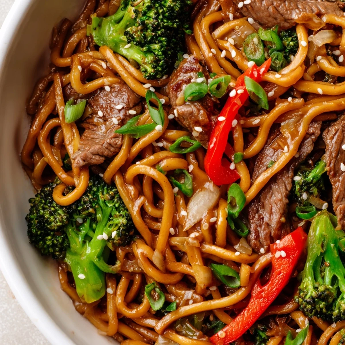 Colorful plate of Beef and Broccoli Lo Mein with Sesame features red bell peppers, green broccoli, and toasted sesame seeds.