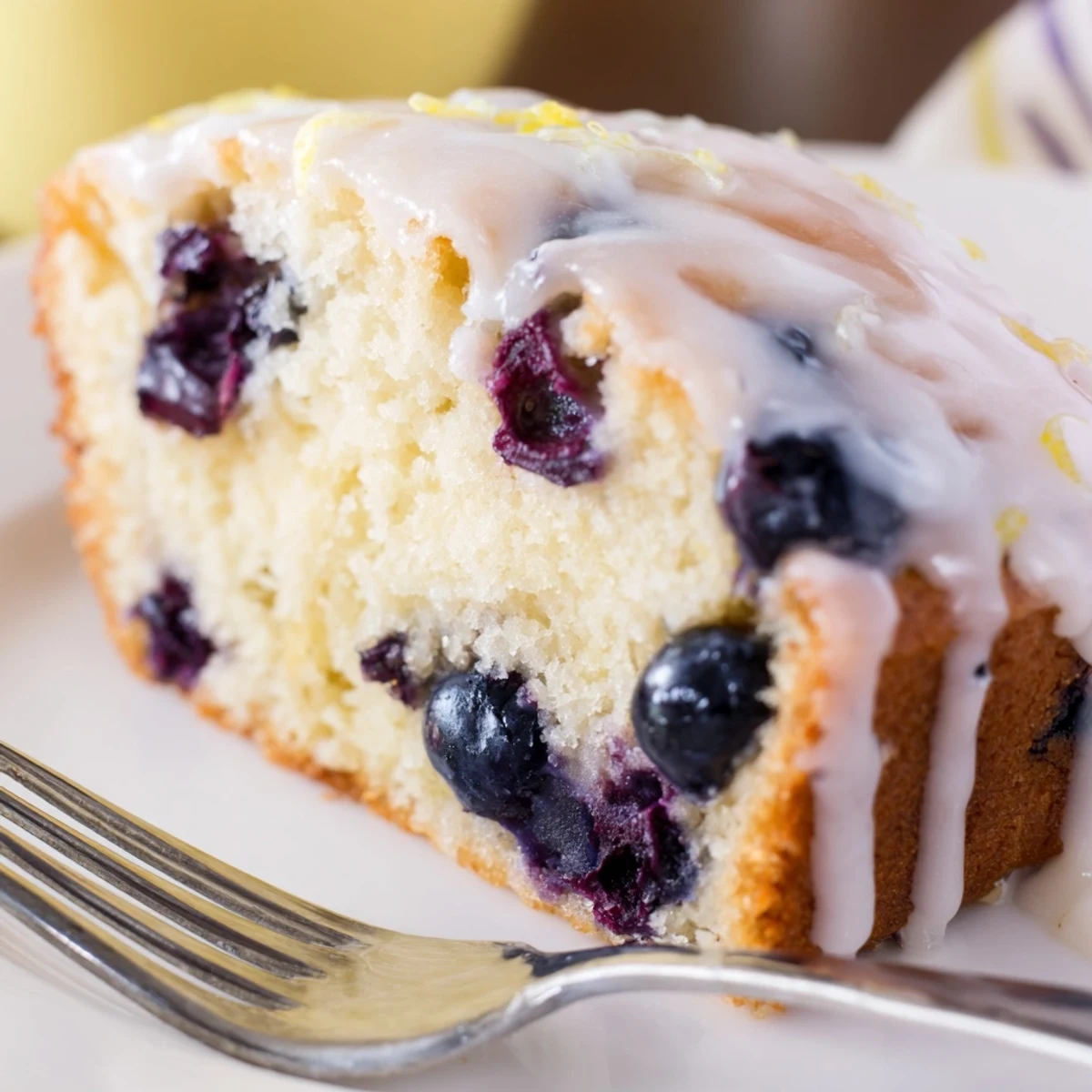A freshly baked Lemon and Blueberry Yogurt Loaf shows a golden crust and vibrant blueberries on a marble counter.