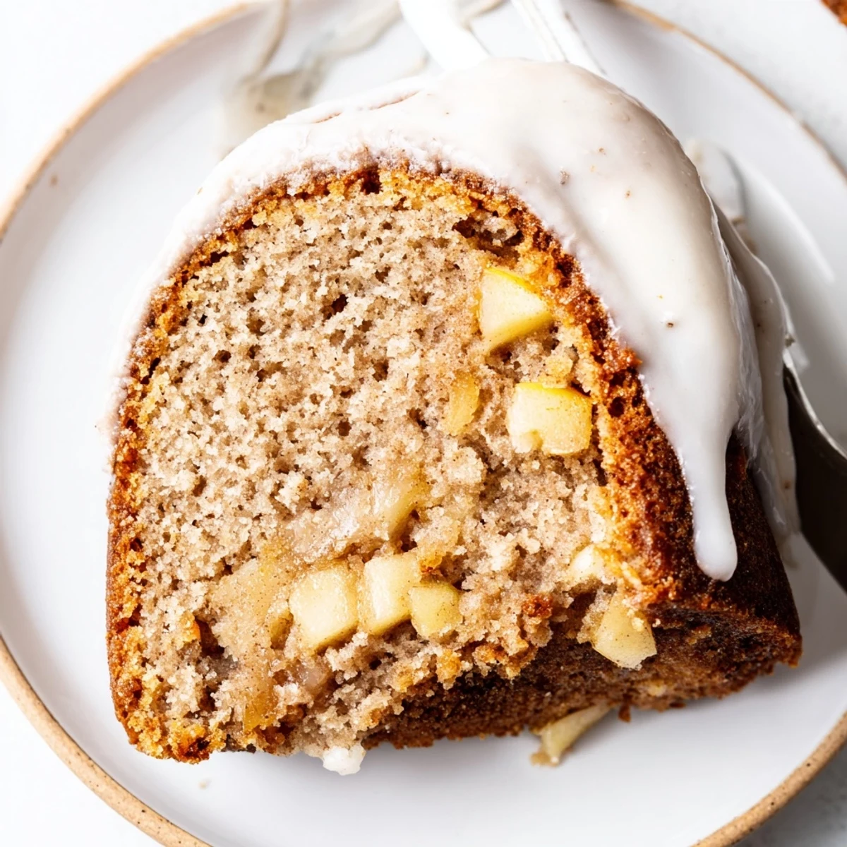 Warm Spiced Apple Cider Bundt Cake served with a dollop of whipped cream for a cozy treat.