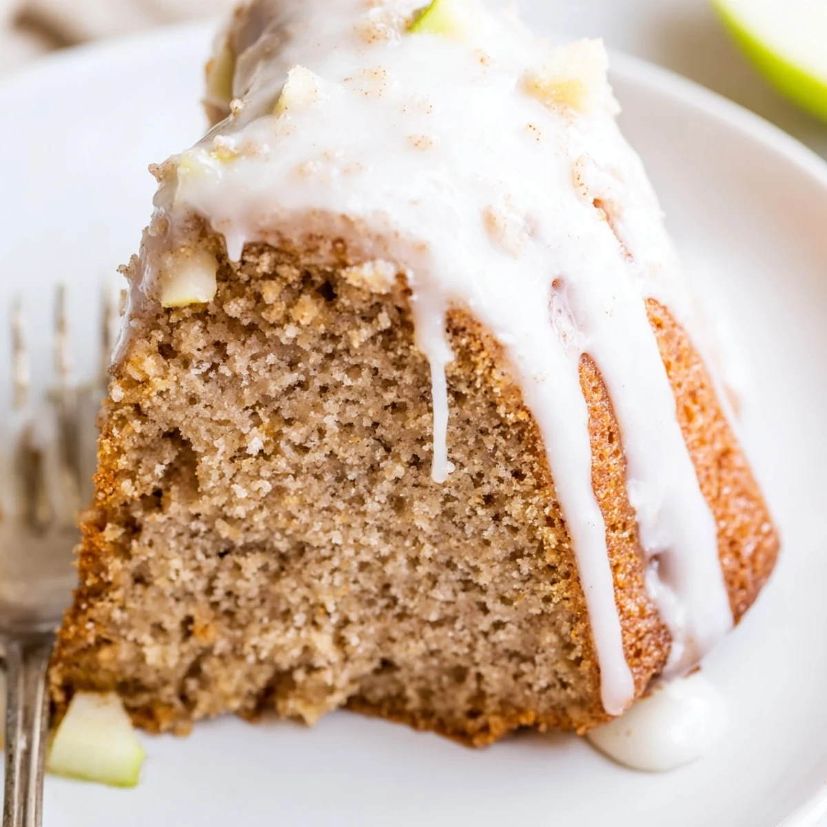 Slice of moist Spiced Apple Cider Bundt Cake drizzled with glaze on a rustic wooden table.