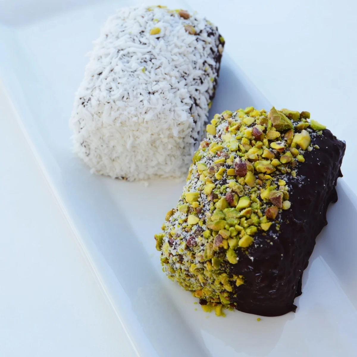 Rustic white plate holding chocolate dipped marshmallows, one with a wooden stick, topped with nuts and coconut.