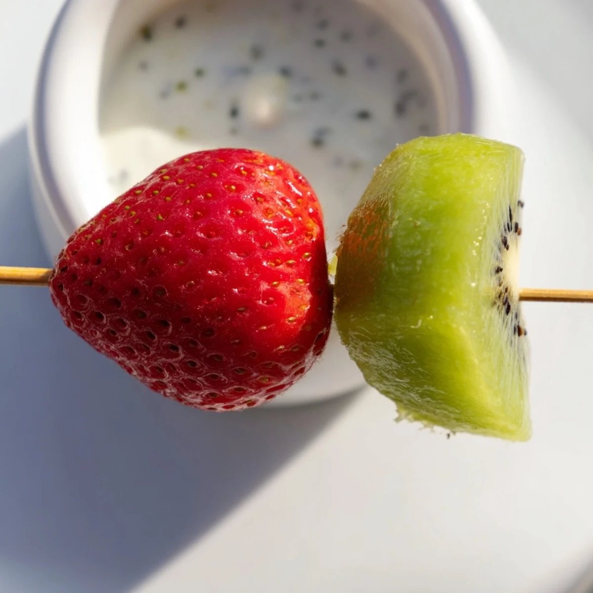 A close-up view of Sweetheart Fruit Kabobs with Yogurt Dip, showing juicy pineapple and grapes alongside a creamy honey-sweetened dip in a small bowl.