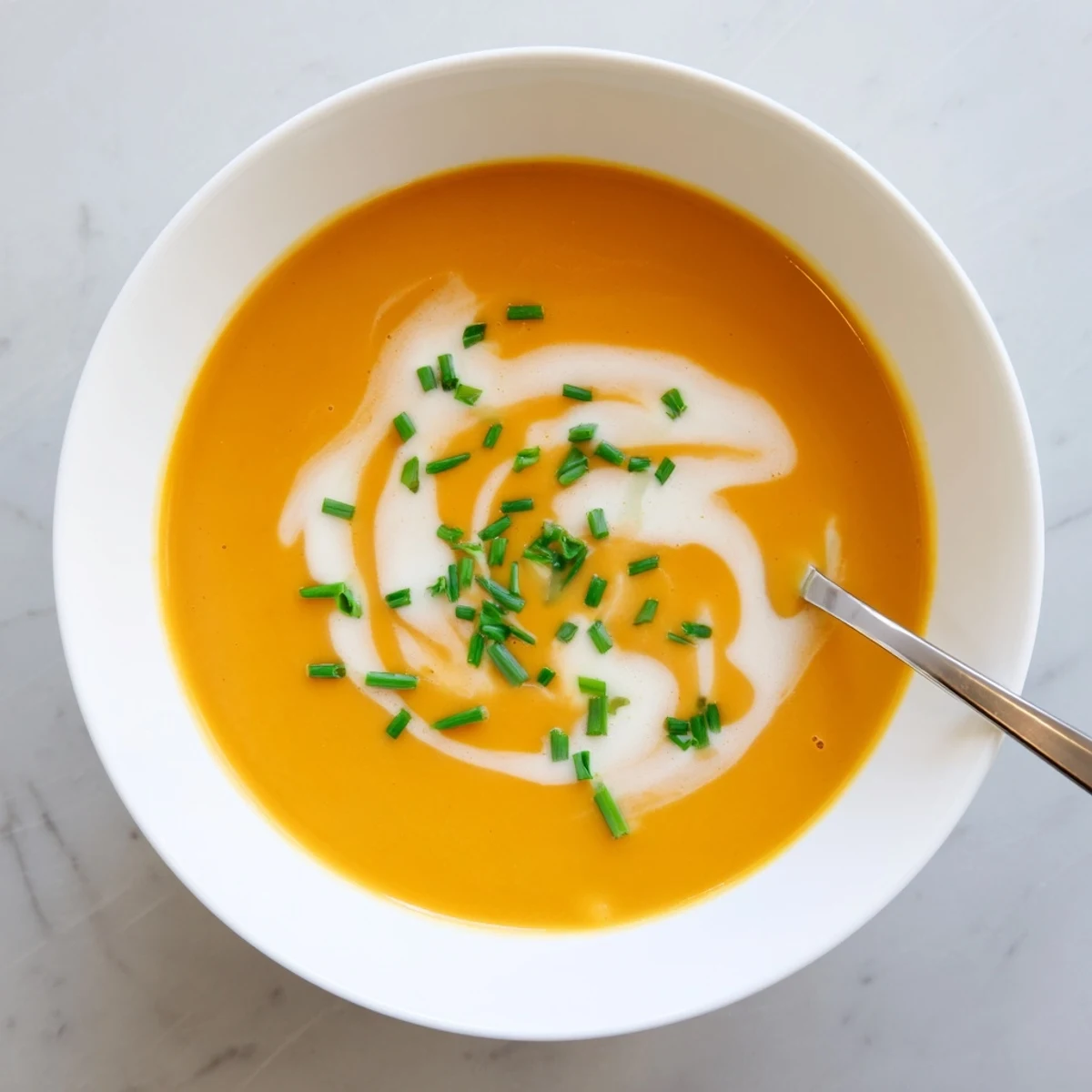 A ladle pours silky Roasted Butternut Squash Soup into a white bowl, with crusty bread on the side.
