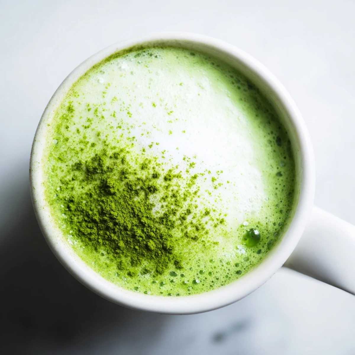 Creamy hot Green Matcha Latte with Almond Milk topped with foam, resting on a rustic wooden coffee shop table.