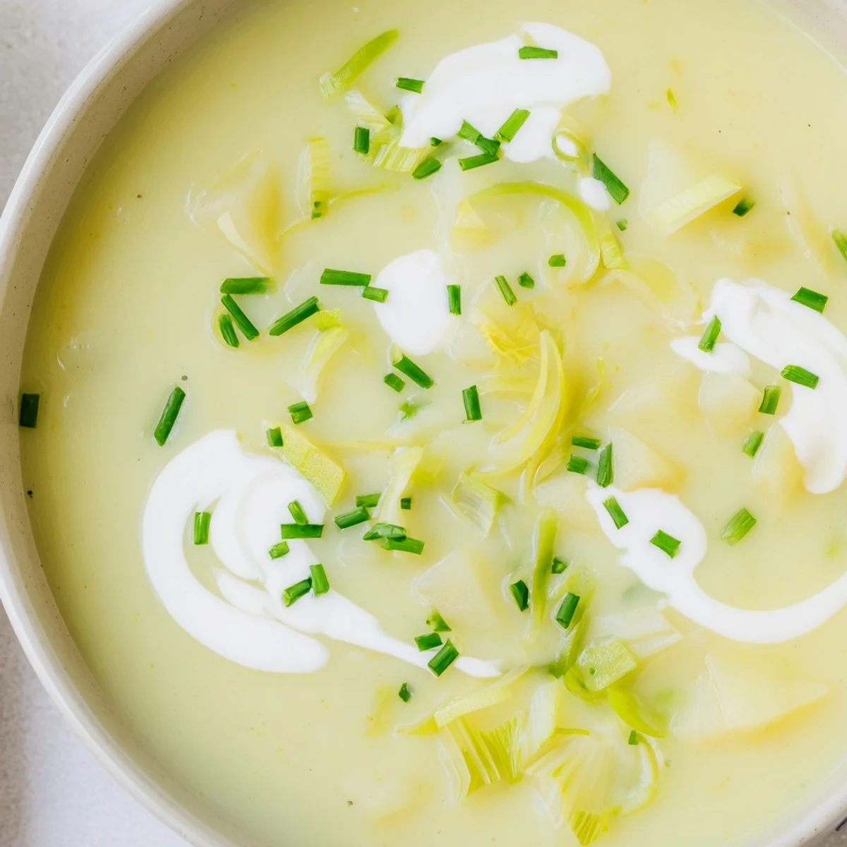 Creamy leek and potato soup served hot in a rustic bowl, garnished with fresh chives and a drizzle of cream.