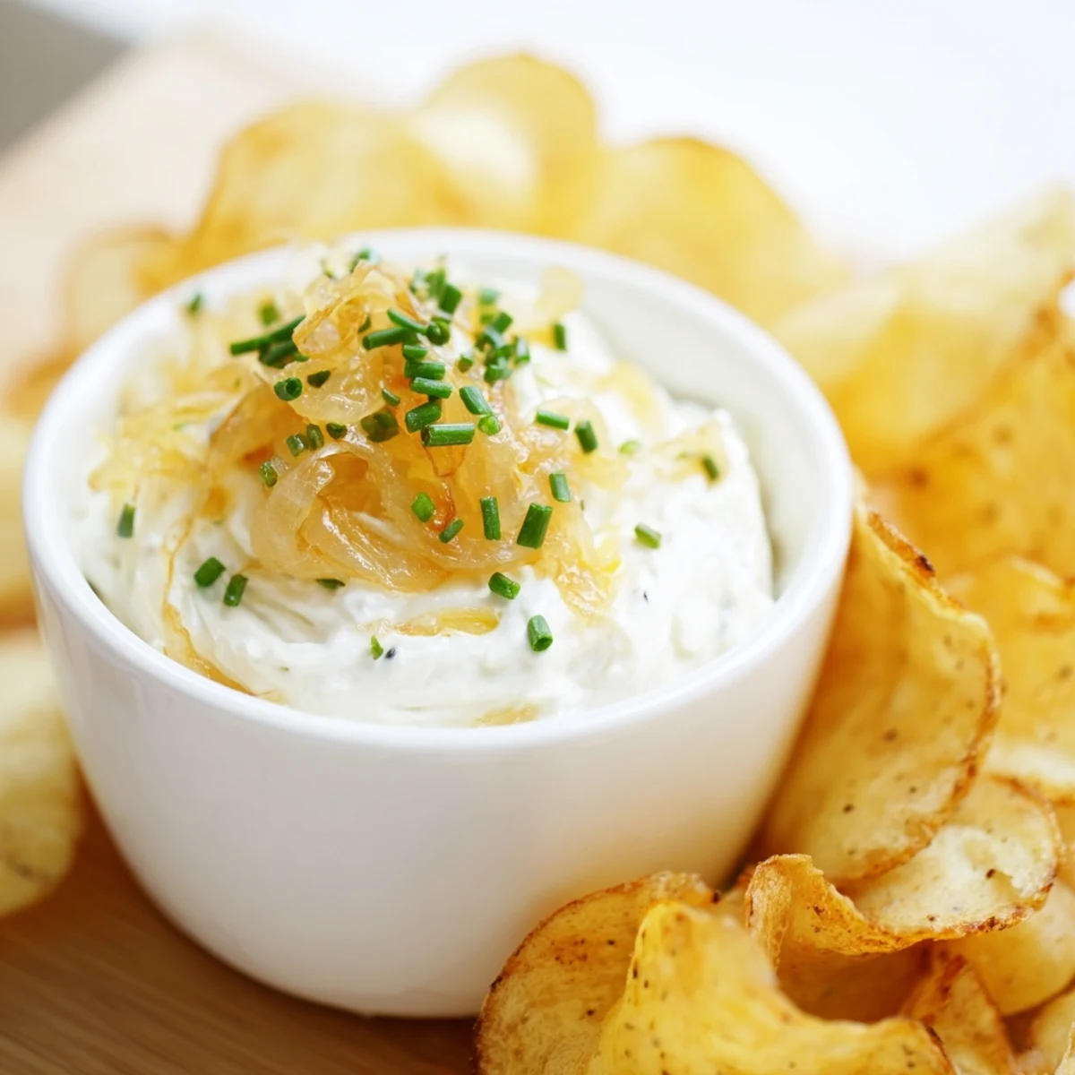 Homemade onion dip with seasoned potato chips, garnished with fresh chives on a platter.