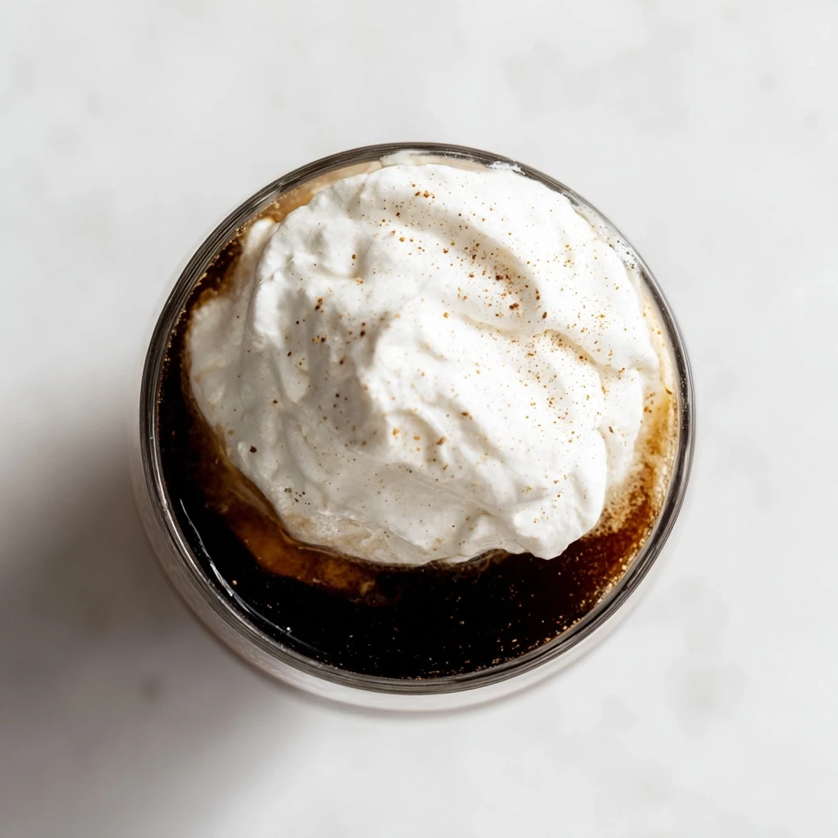 Steaming hot coffee topped with fluffy whipped cream in a glass, a classic Irish Coffee Mocktail garnished with nutmeg.