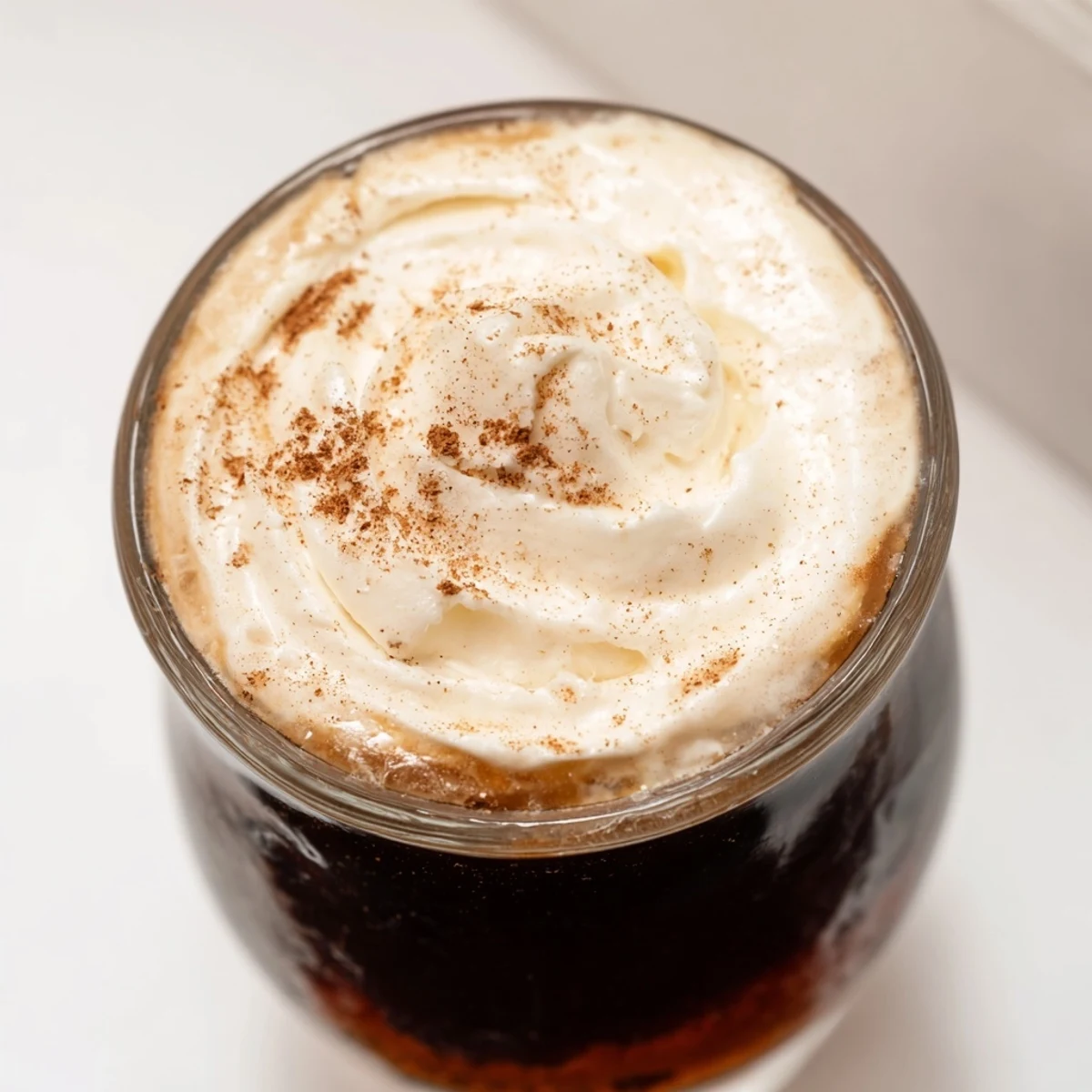 Close-up view of a creamy Irish Coffee Mocktail, showing the rich brown sugar and thick vanilla-scented whipped cream.