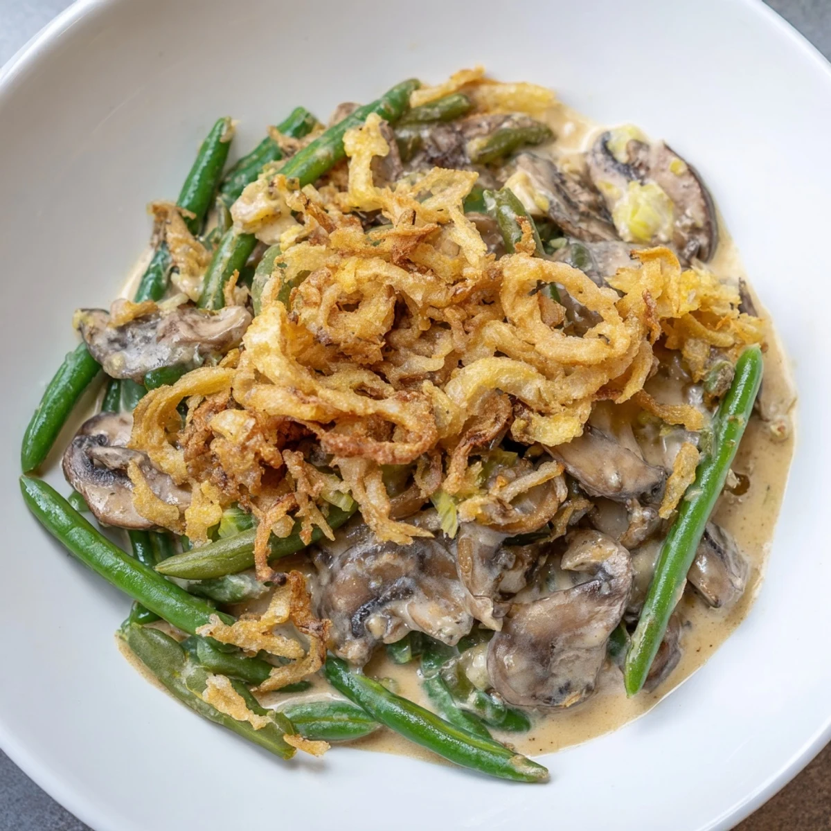 Green Bean Casserole with Crispy Onions served in a white dish, paired with roast chicken and mashed potatoes for a classic American dinner.