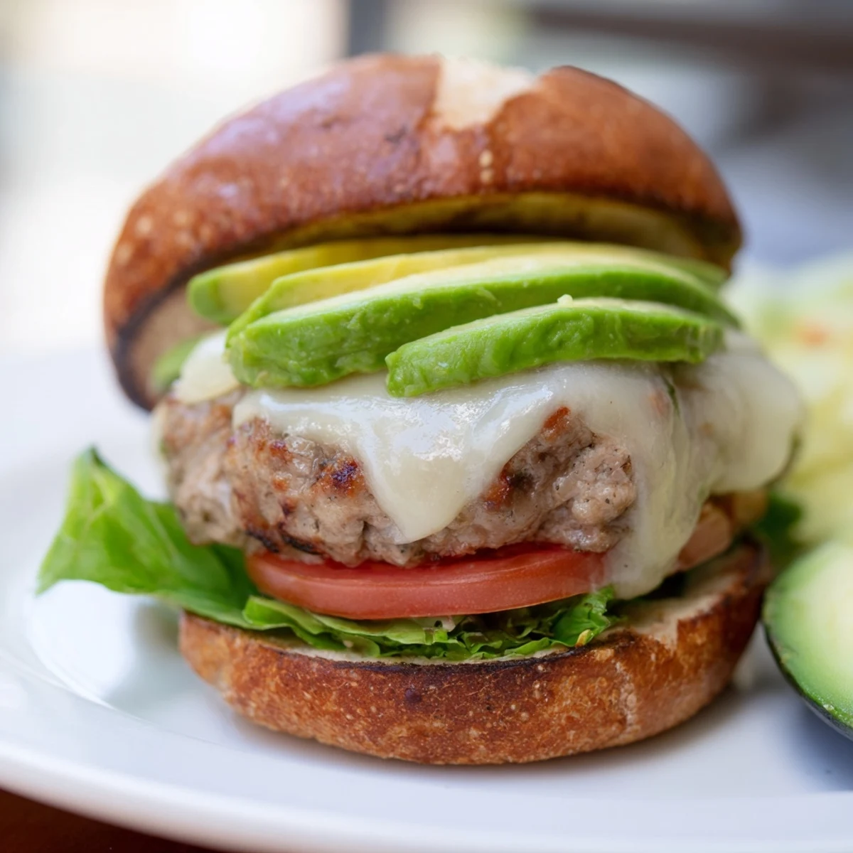 Golden brown turkey burger with melted Swiss cheese and creamy avocado slices on a toasted whole wheat bun, garnished with fresh lettuce and tomato.