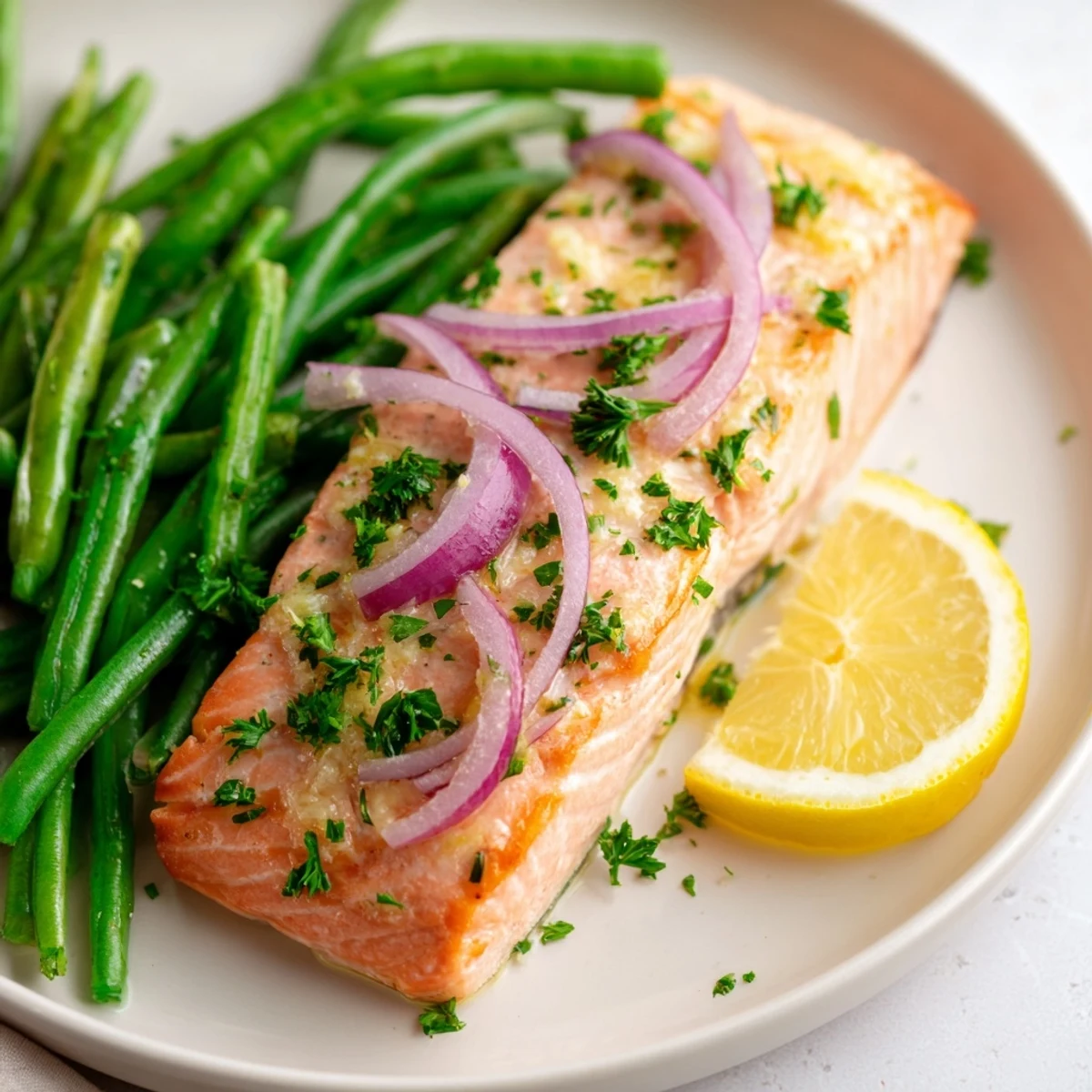 Tender salmon fillets and crisp green beans on a sheet pan, garnished with fresh parsley and lemon wedges.