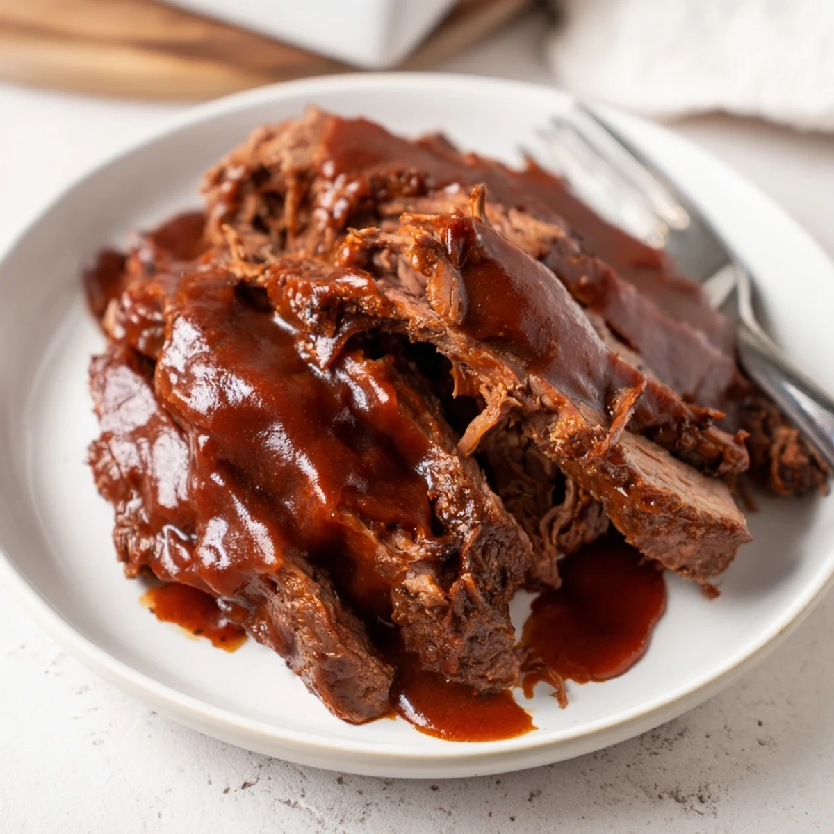 A fork tender Slow Cooked Beef Brisket with BBQ Sauce sits on a cutting board next to a bowl of extra sauce.