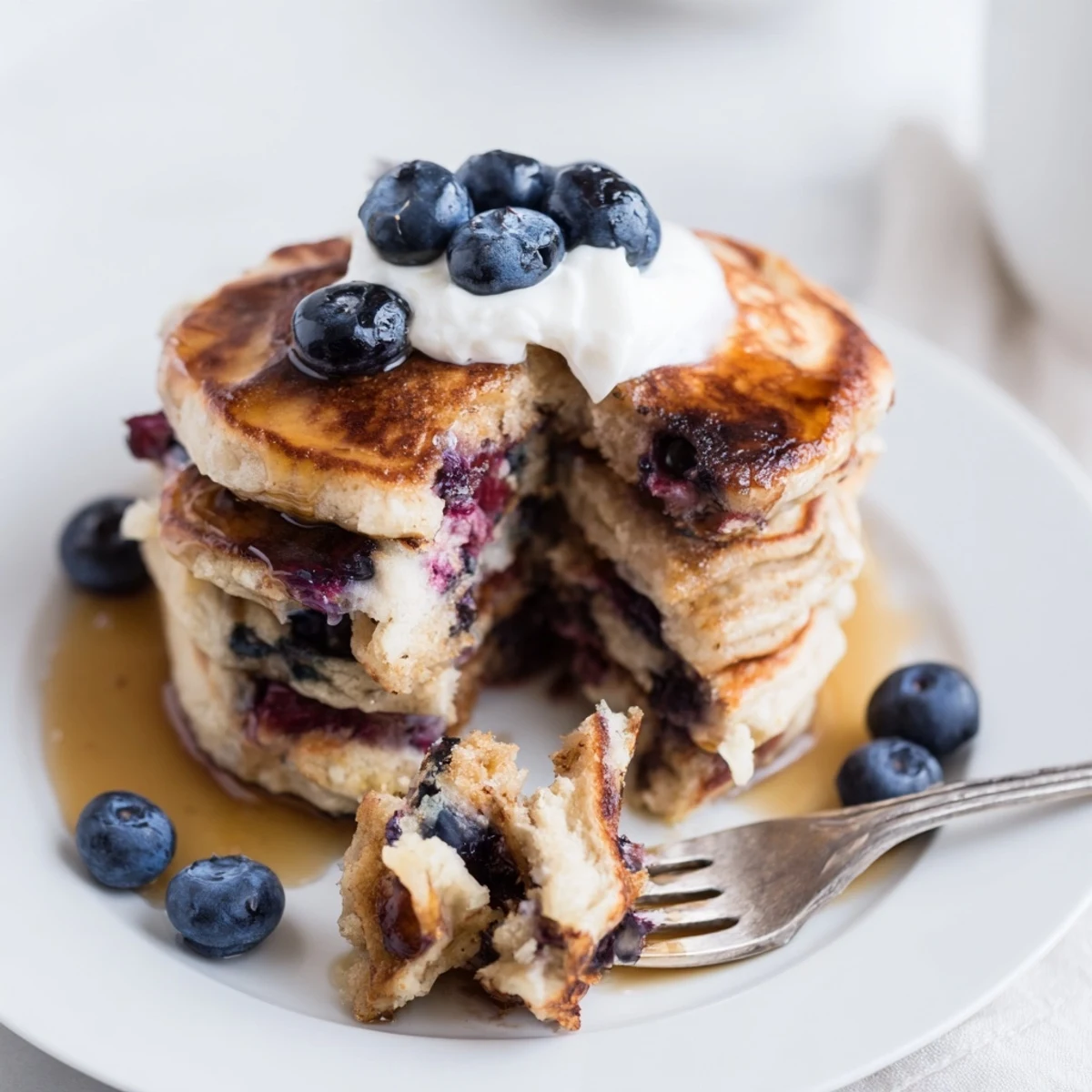 Golden-brown Fluffy Greek Yogurt Blueberry Pancakes served on a rustic table with yogurt dollop and berries.
