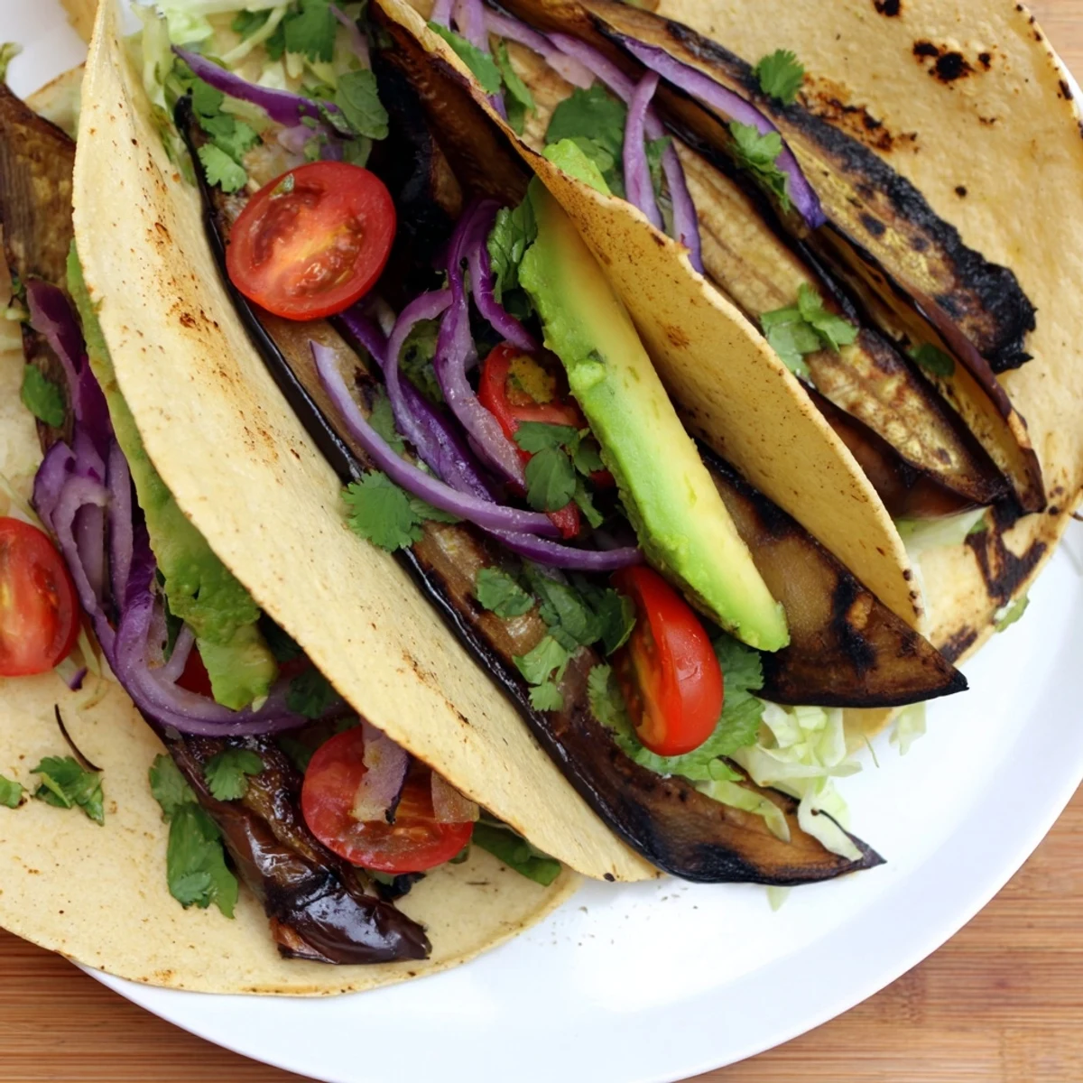 Charred Eggplant Tacos displayed in warm corn tortillas topped with fresh lettuce, tomatoes, and avocado.