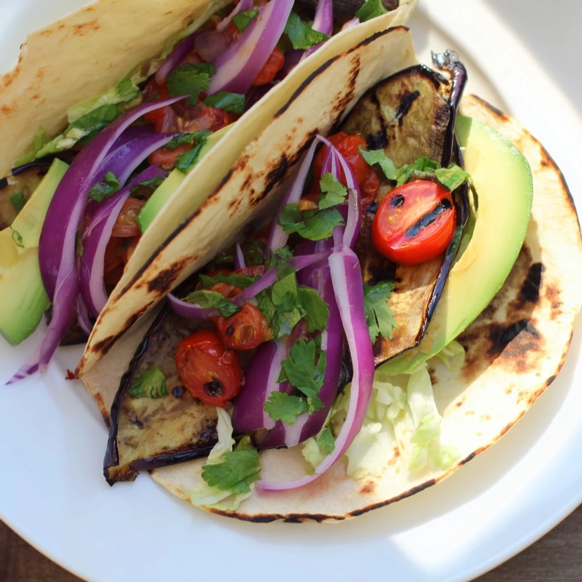 Vibrant vegan Charred Eggplant Tacos served on a plate with red onion and cherry tomatoes.