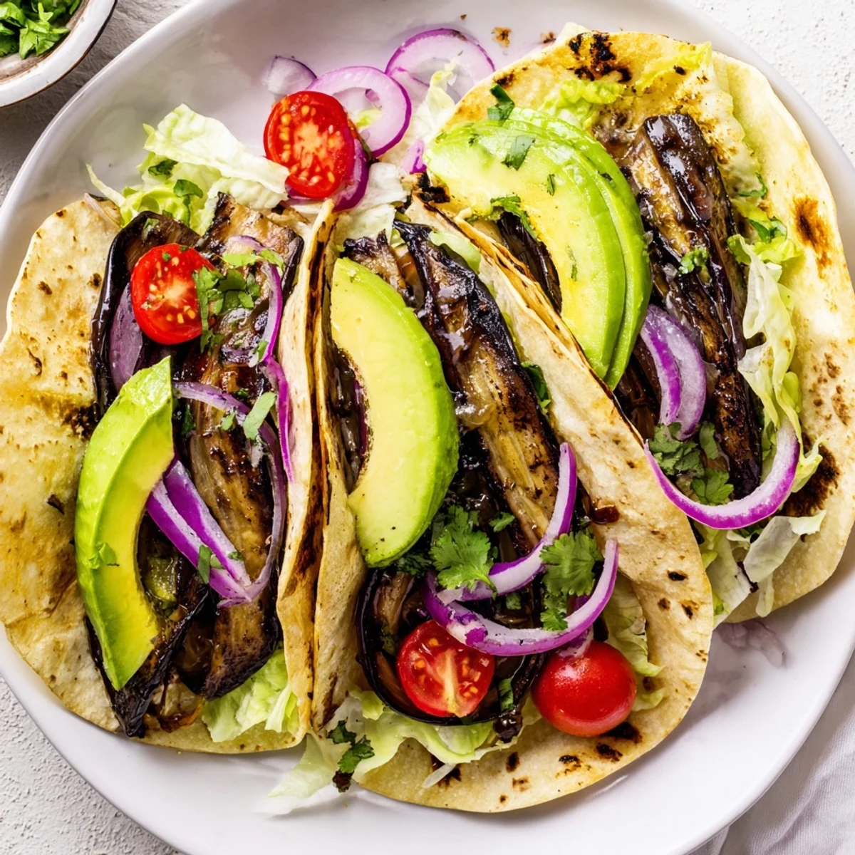 A close-up of smoky grilled eggplant slices inside Charred Eggplant Tacos with cilantro and lime wedges.