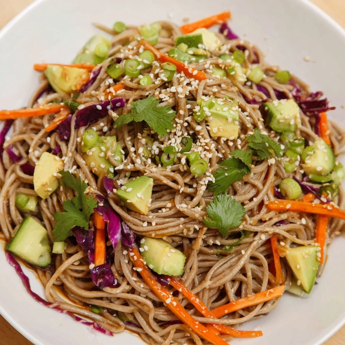 Vibrant Sesame Avocado and Soba Noodle Salad served in a white bowl, garnished with sesame seeds and fresh green onions.