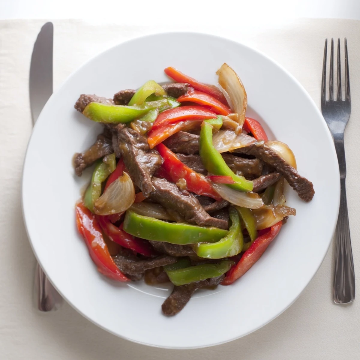 A close-up of Sizzling Chinese Pepper Steak with Onions, glistening with savory sauce beside fluffy rice and chopsticks ready for serving.