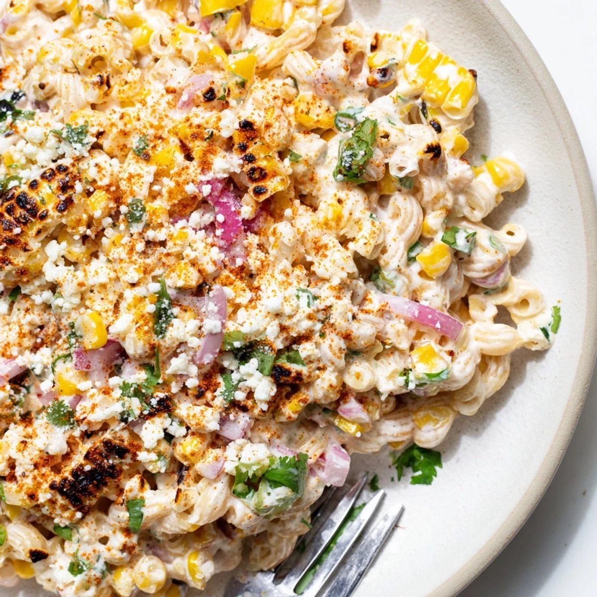 Bright Mexican Street Corn Pasta Salad in a white bowl, featuring charred corn, diced peppers, and crumbled cotija cheese garnish.