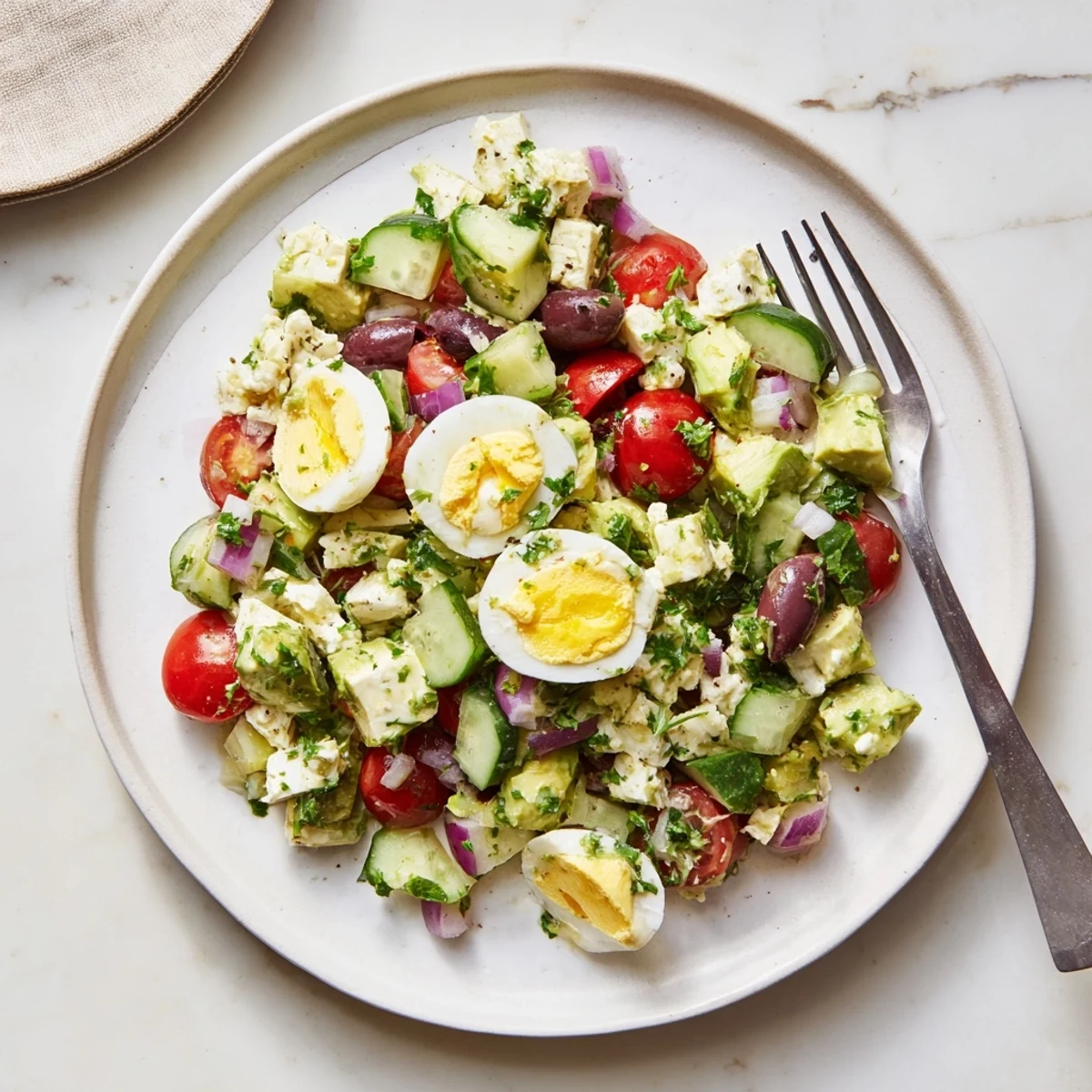 Creamy Mediterranean avocado egg salad featuring bright cherry tomatoes, cucumber, and Kalamata olives in a lemon herb dressing