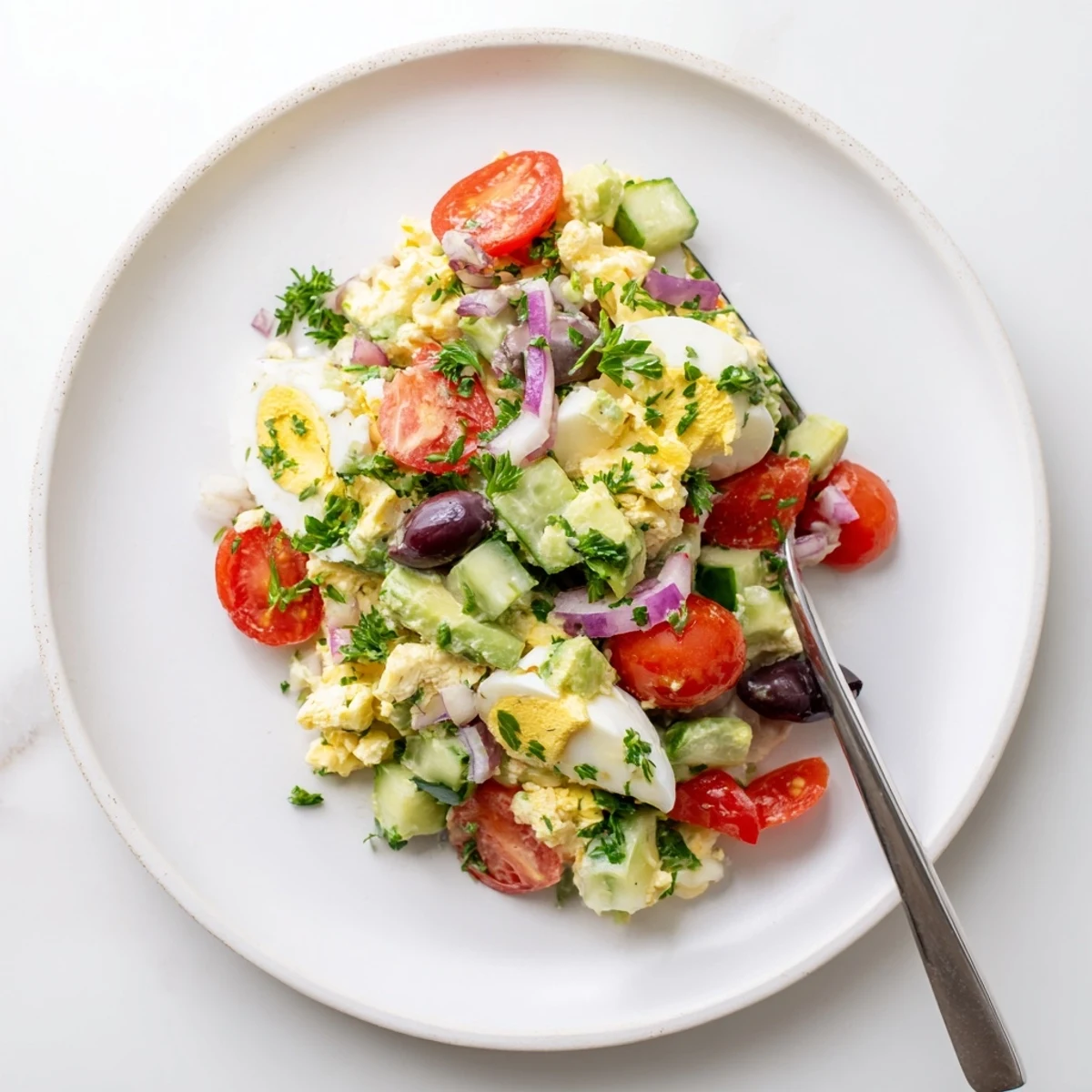 Vibrant bowl of zesty avocado egg salad dotted with red onion, parsley, and crisp vegetables for a refreshing lunch