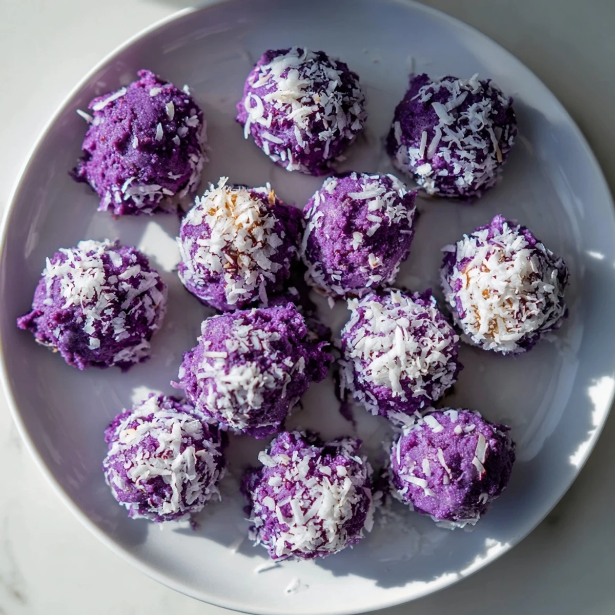 Vibrant purple Coconut Ube Besito cookies rolled in shredded coconut arranged on parchment paper
