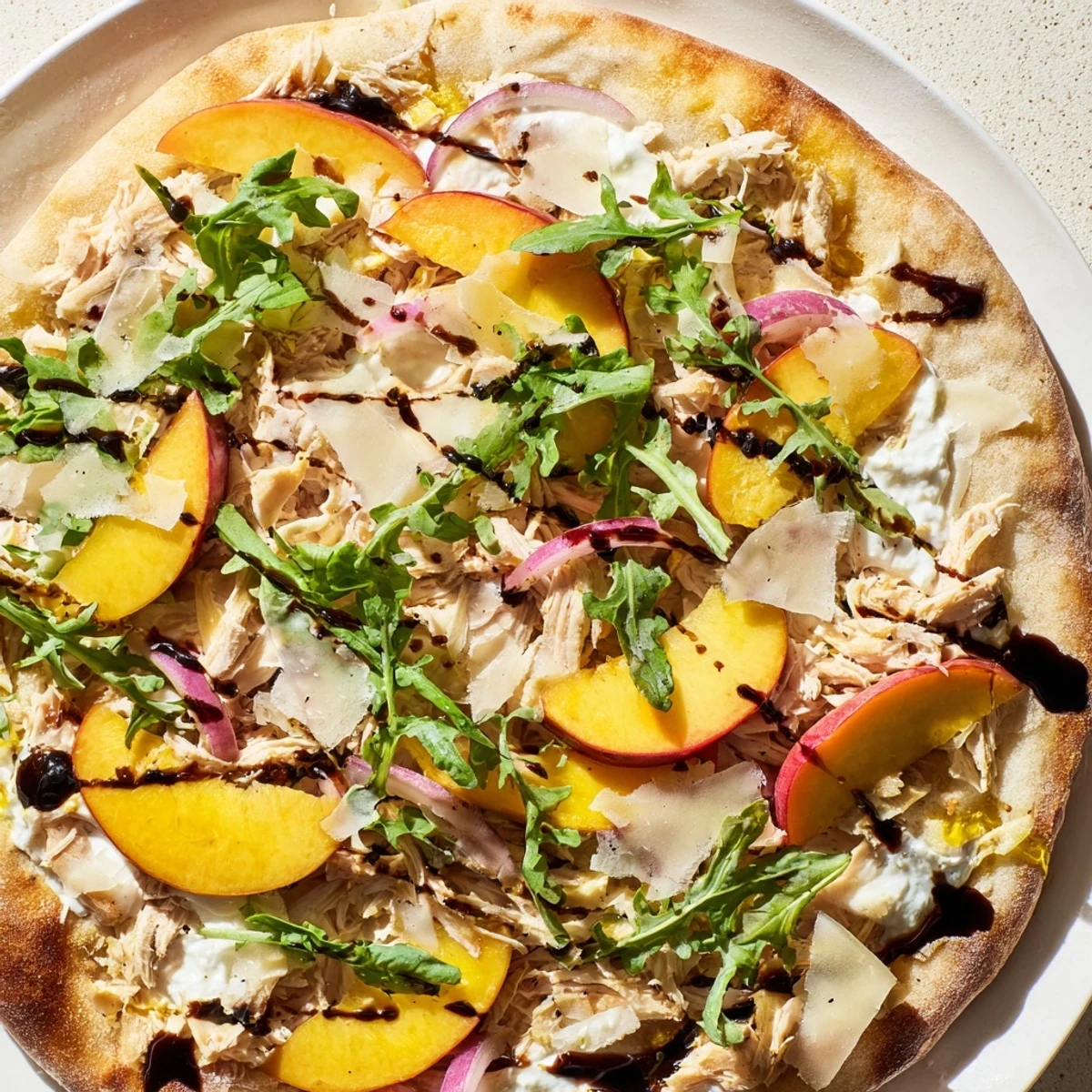 Golden chicken peach ricotta pizza topped with fresh arugula and balsamic glaze