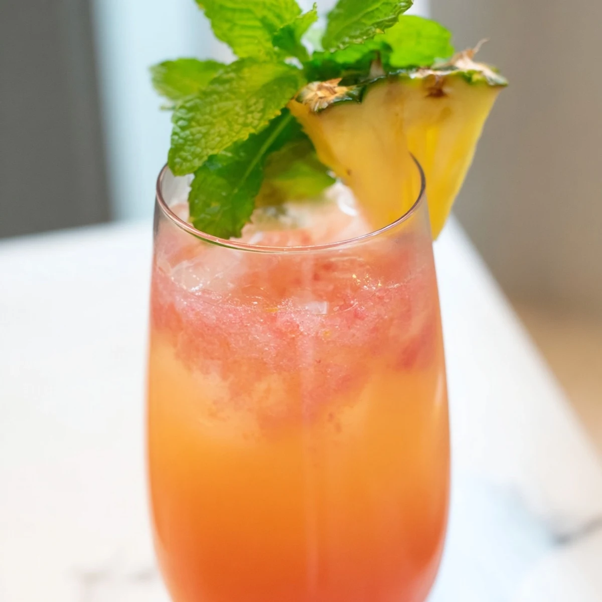 Vibrant pink pitcher filled with pineapple pink lemonade and floating ice on wooden counter