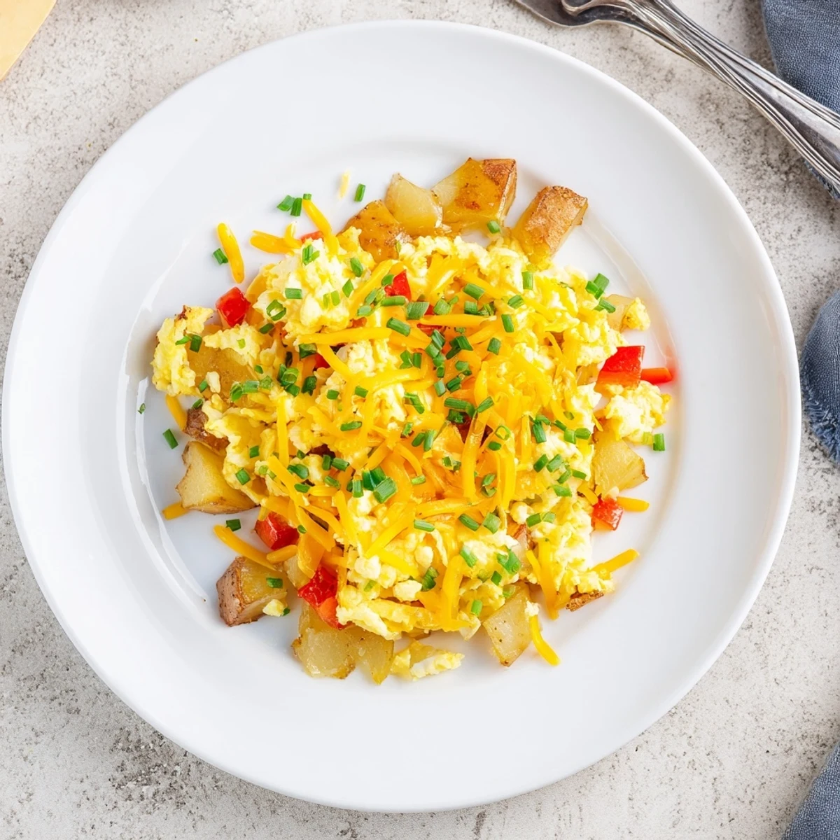 Hearty breakfast skillet of cheesy potato egg scramble topped with fresh chives and red bell peppers
