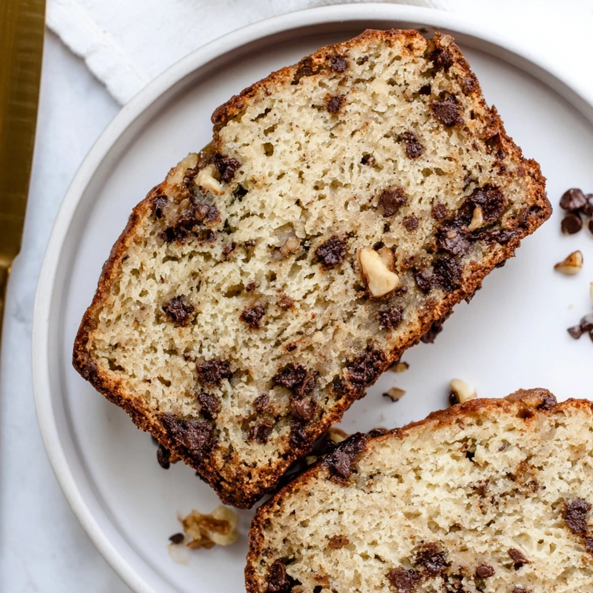 Warm slice of homemade chocolate chip banana bread topped with extra chocolate chips and served on a white plate