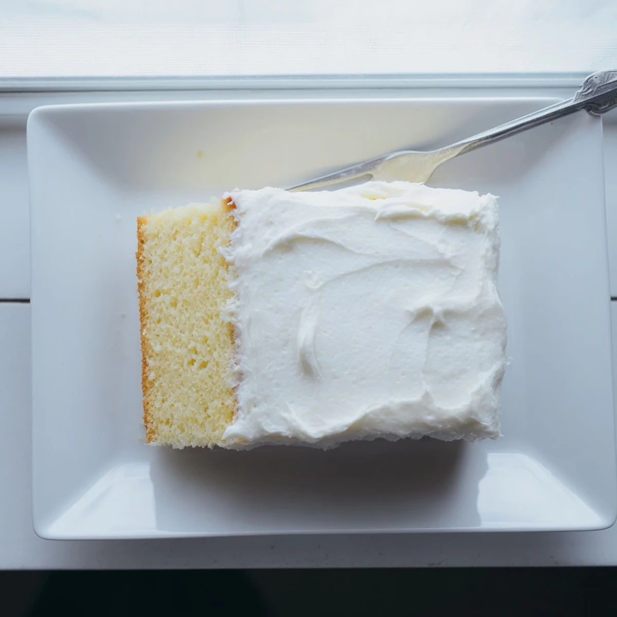 Golden slice of fluffy church cake topped with creamy white vanilla frosting