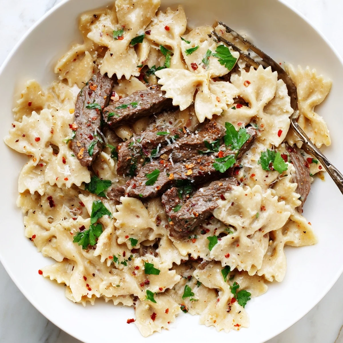 Golden bowtie pasta coated in zesty cream cheese Alfredo topped with seasoned sliced beef strips