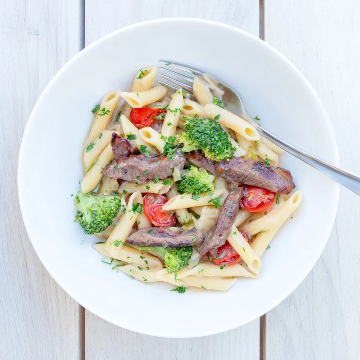 Hearty plate of creamy garlic steak penne tossed with sliced sirloin, broccoli, and burst cherry tomatoes in white sauce