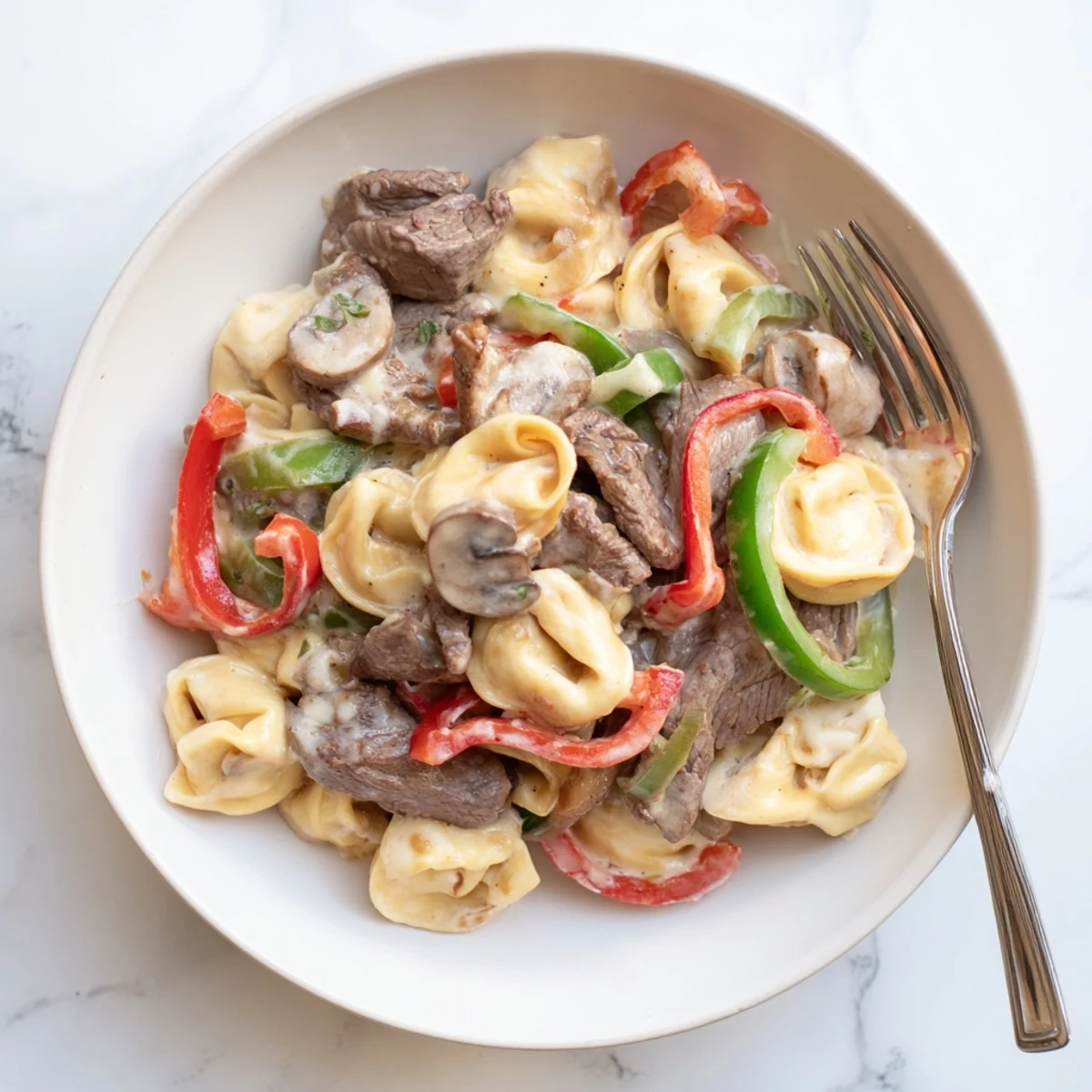 Hearty slow cooker cheesesteak tortellini featuring colorful peppers, onions, and savory beef in a cheesy cream sauce
