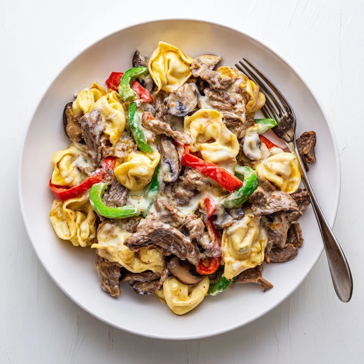 Bowl of cheesy Crock Pot Cheesesteak Tortellini topped with extra mozzarella and garnished with fresh parsley