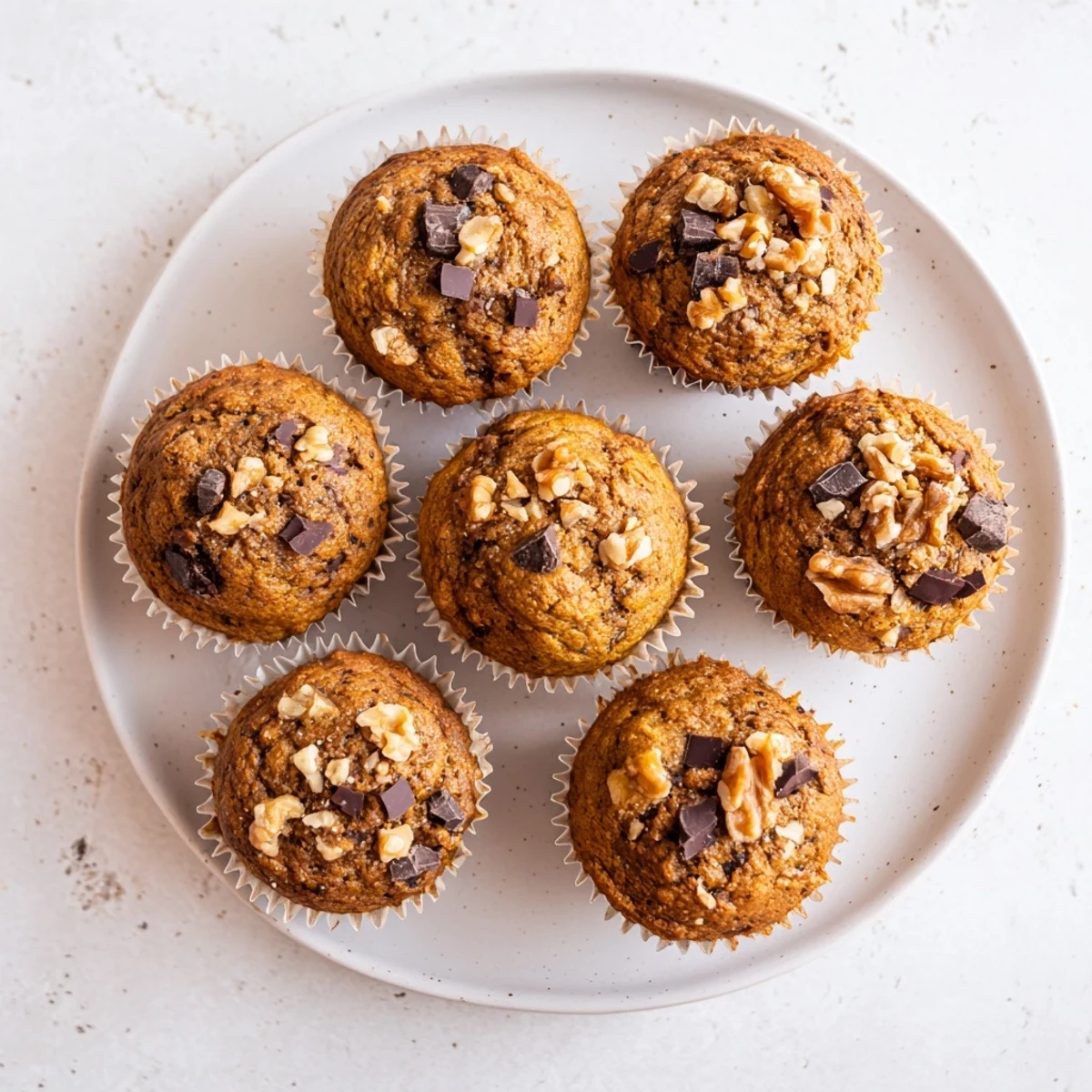 Golden brown pumpkin banana muffins topped with walnuts on a wooden board, ready for breakfast