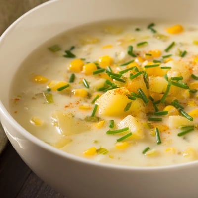 Hearty creamy corn chowder with tender potatoes, served steaming in a rustic bread bowl for a cozy meal.  