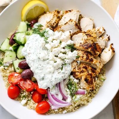 Golden seared Greek Chicken Grain Bowl nestled over fluffy grains with roasted vegetables