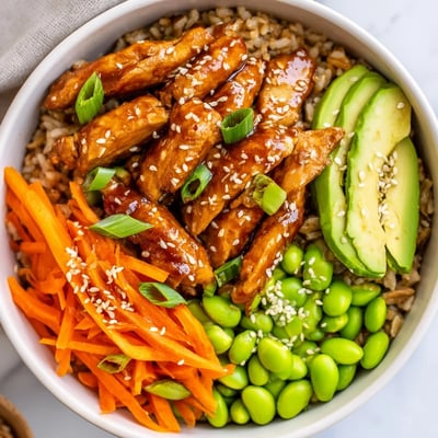 Steaming teriyaki chicken grain bowl with colorful vegetables on fluffy brown rice